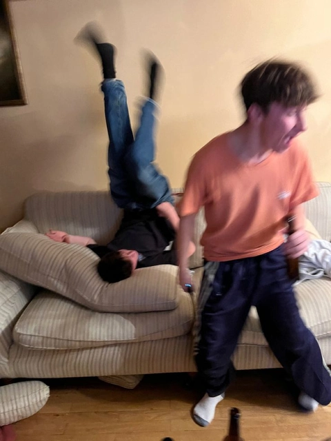 A man standing on top of a couch next to a child.