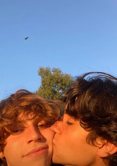A couple of people that are kissing in front of a tree.