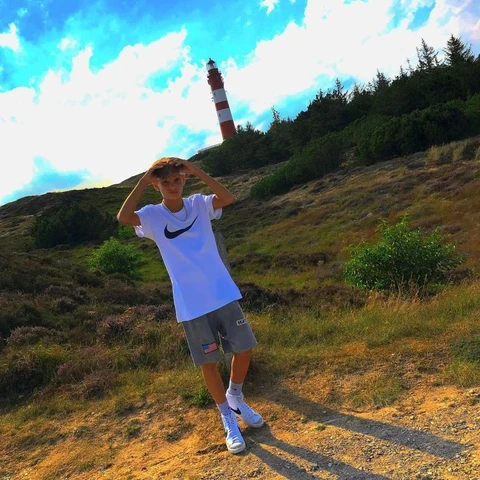 A young boy standing on top of a hill next to a lighthouse.