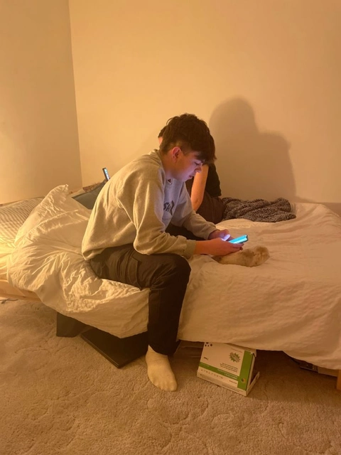 A man sitting on top of a bed holding a cell phone.