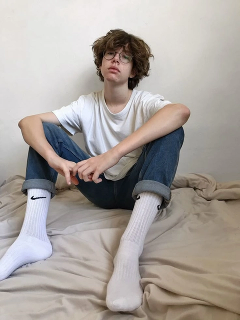 A young man sitting on top of a bed with his legs crossed.