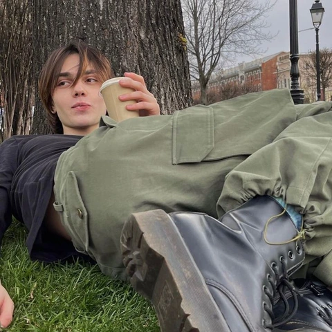 A man laying on the grass with a cup of coffee.