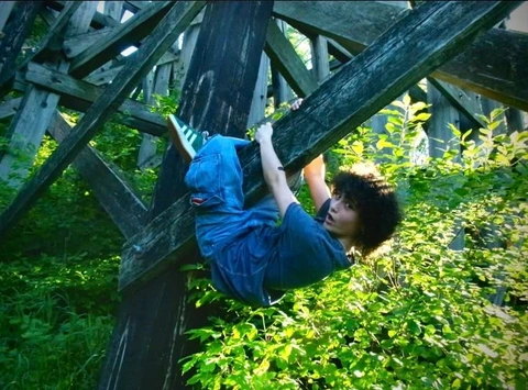 A young boy hanging upside down from a wooden structure.