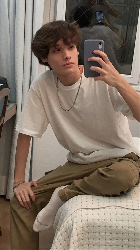 A young man sitting on a bed taking a selfie.