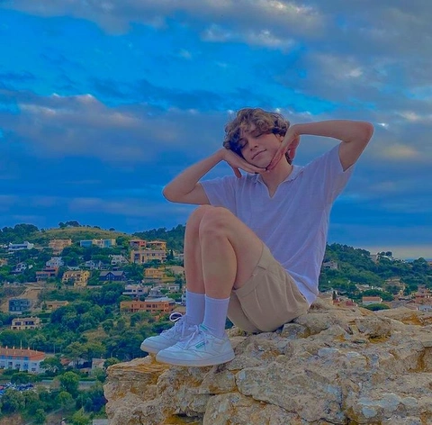 A man sitting on top of a rock with his hands on his head.