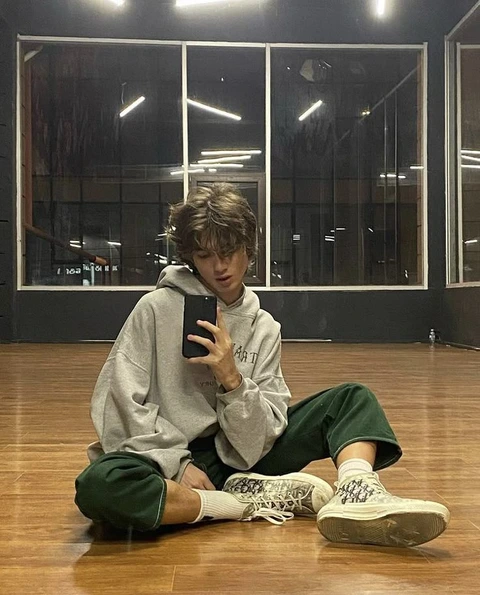 A young man sitting on the floor looking at his cell phone.