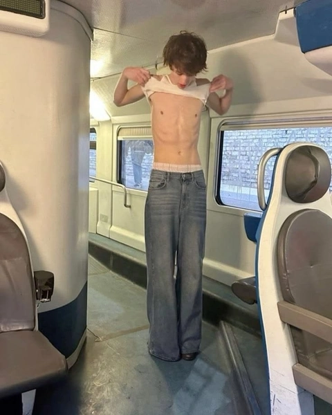 A shirtless man standing in the middle of a train.