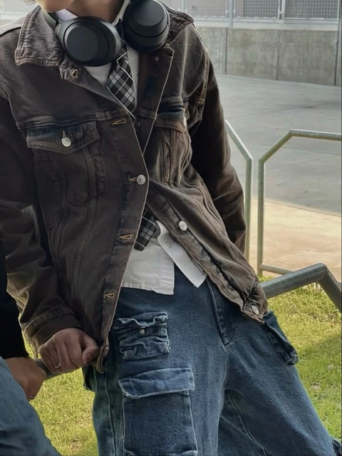 A man wearing a jacket and headphones standing in front of a fence.
