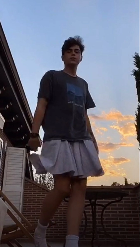 A young man in a skirt and t-shirt standing on a set of stairs.