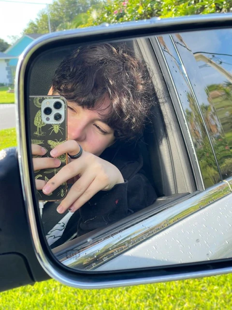 A young man taking a picture of himself in a car mirror.
