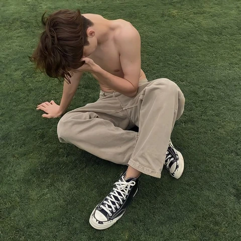 A shirtless man and a woman sitting on the grass.