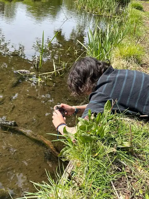 A man sitting on a log in the grass next to a pond.