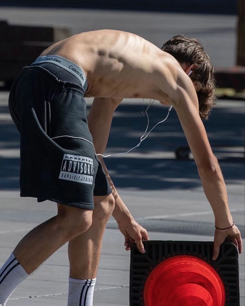 A shirtless man standing next to a speaker on a street.
