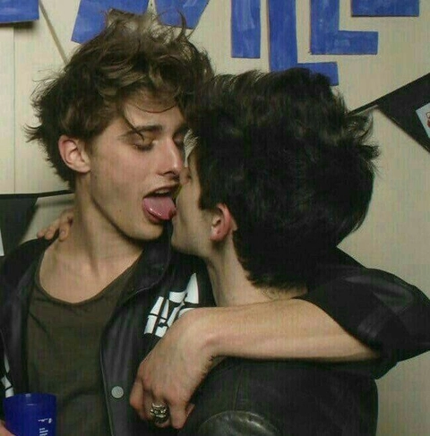 A group of young men kissing each other in front of a wall.