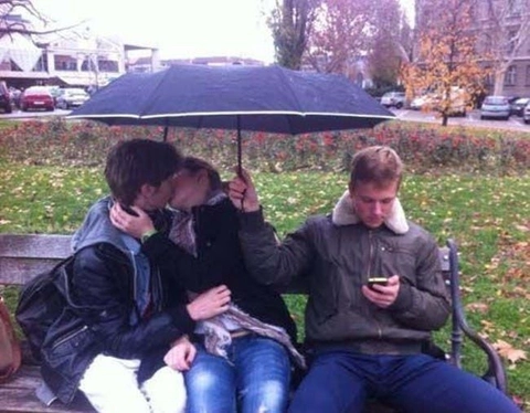 A group of people sitting on a bench under an umbrella.