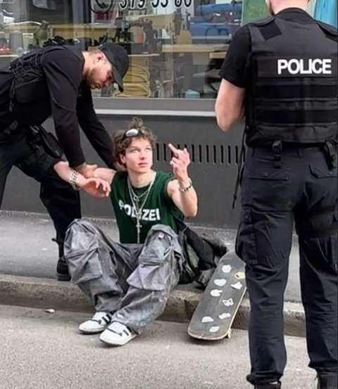 A young man sitting on the ground next to a police officer.