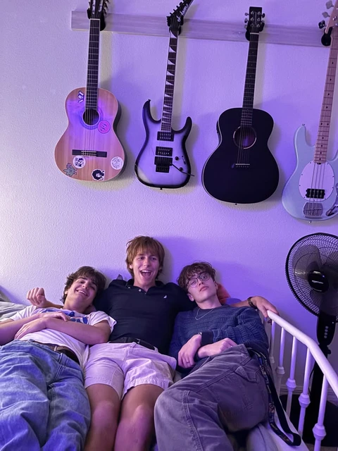 A group of young men sitting on top of a bed next to guitars.