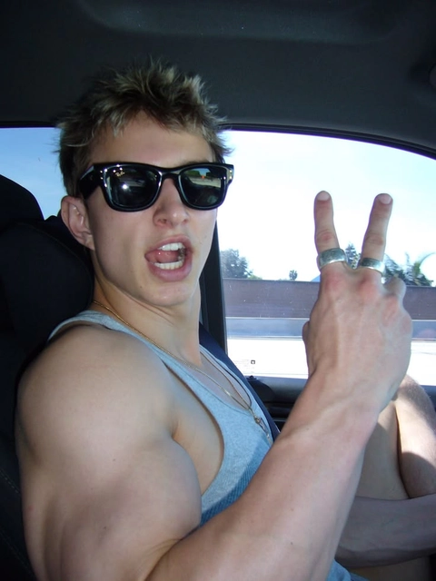 A shirtless man wearing sunglasses sitting in the back seat of a car.