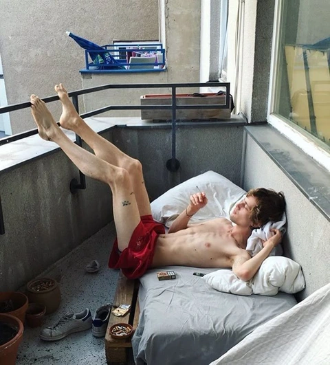 A man laying on top of a bed next to a window.