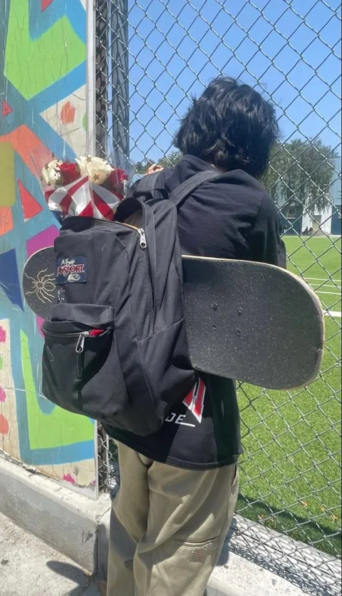 A man with a skateboard leaning against a fence.